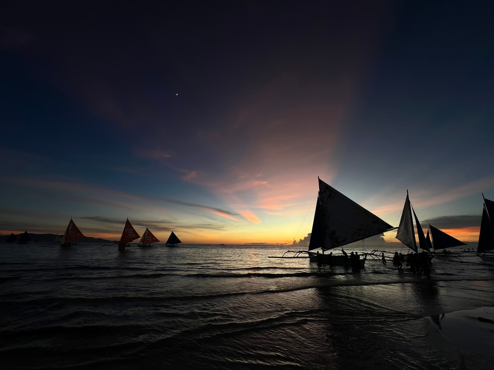 Silhouette de voiliers au coucher du soleil sur l'océan.