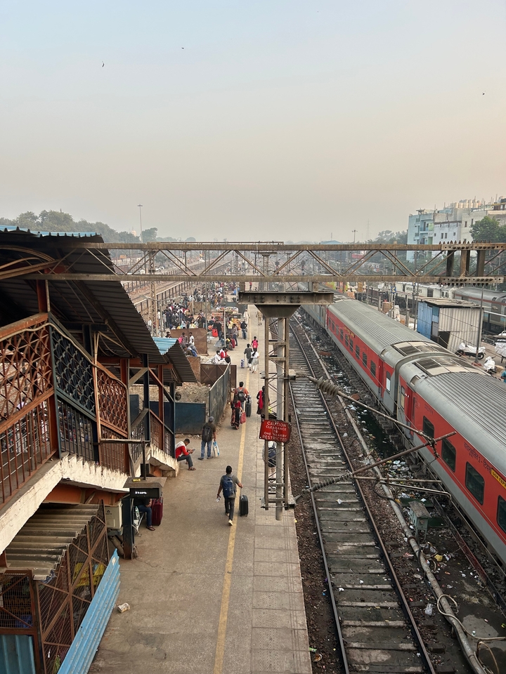 Gare ferroviaire bondée avec des gens et un train rouge visible.