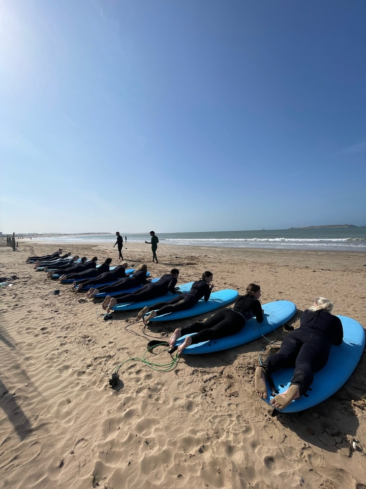 Menschen in Neoprenanzügen, die auf Surfbrettern an einem Sandstrand liegen.
