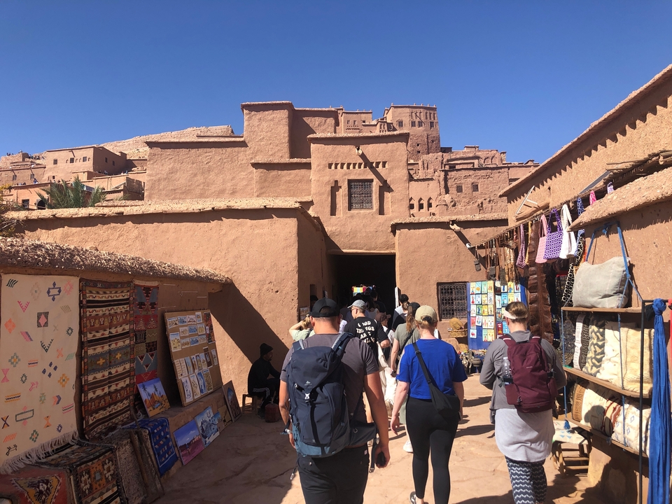 Touristen, die durch einen Markt mit traditionellen Gebäuden gehen.