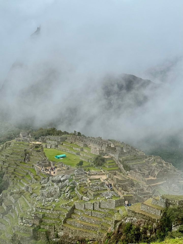 Weite Sicht auf Machu Picchu mit Nebel und entfernten Menschen.