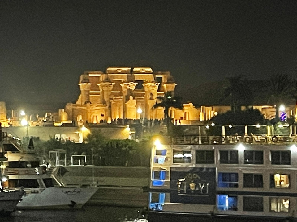 Structure de temple illuminée la nuit avec des bateaux au premier plan.