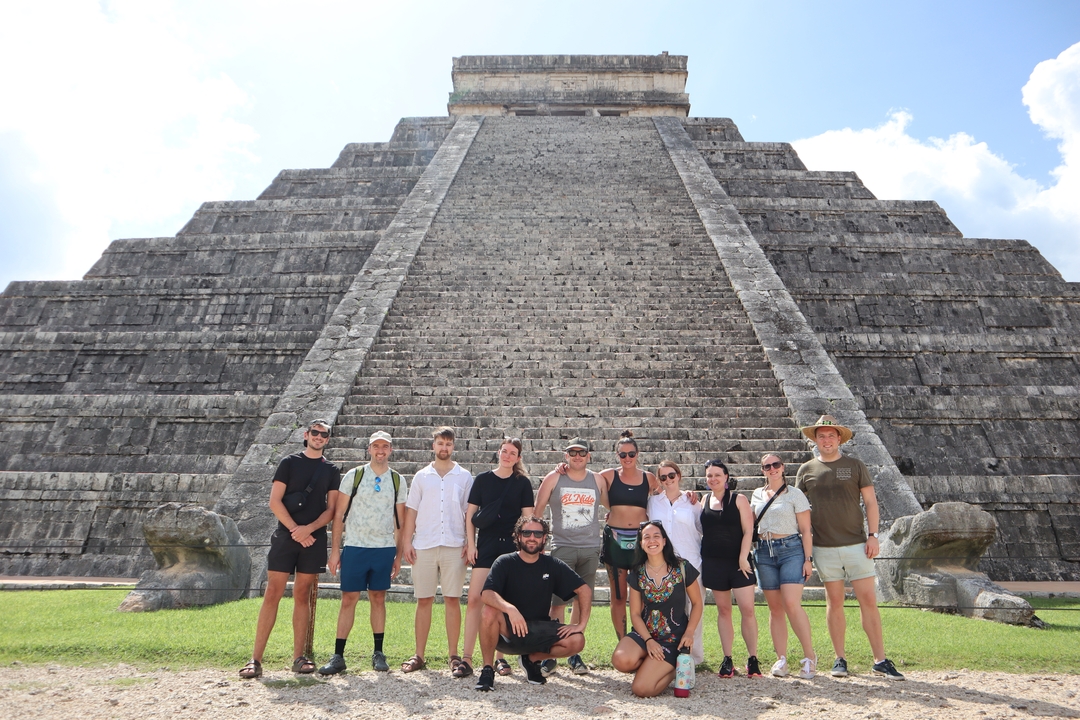 Groupe de touristes posant devant une grande pyramide.