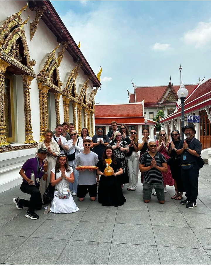 Un groupe debout en tenue traditionnelle avec une architecture de temple.