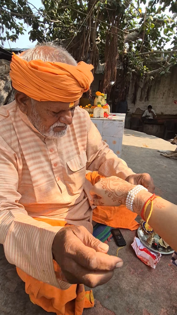 Vieil homme attachant un fil sacré au poignet d'une personne.