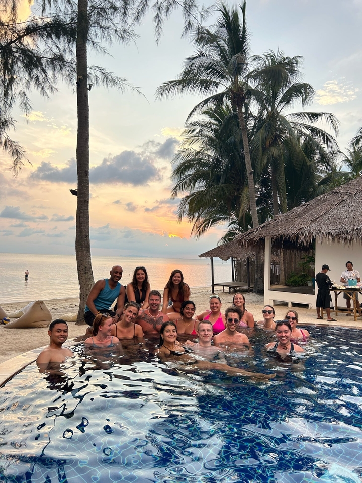 Groupe au bord d'une piscine en bord de mer avec des huttes au toit de chaume au coucher du soleil.