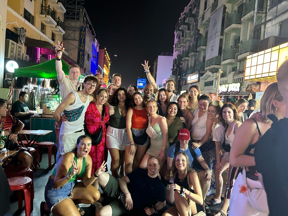 Large group of people posing at a vibrant street market or festival at night.
**French translation:**
Grand groupe de personnes posant dans un marché de rue animé ou un festival nocturne.