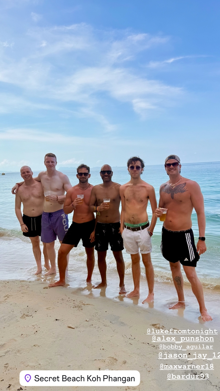 Groupe d'amis posant torse nu sur une plage avec des boissons.