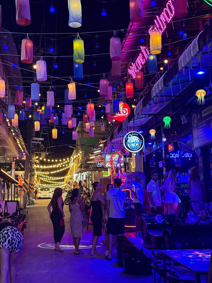 Scène de rue animée avec des lumières et des enseignes colorées.