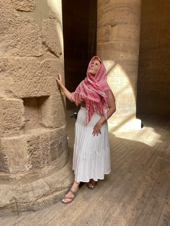 Personne dans un temple portant un foulard rouge et blanc avec des sculptures anciennes sur le mur.