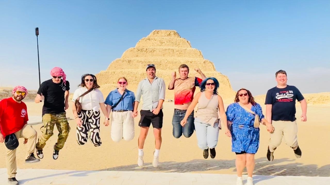 Groupe de personnes sautant devant une pyramide à degrés.