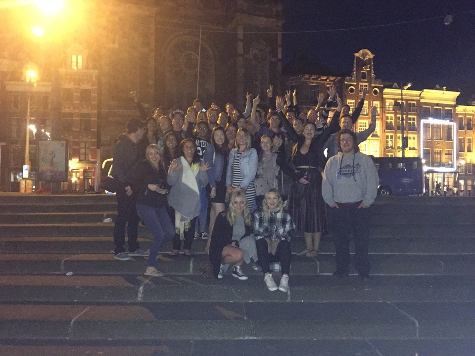 Grand groupe de personnes posant ensemble la nuit dans un environnement urbain avec des bâtiments éclairés.