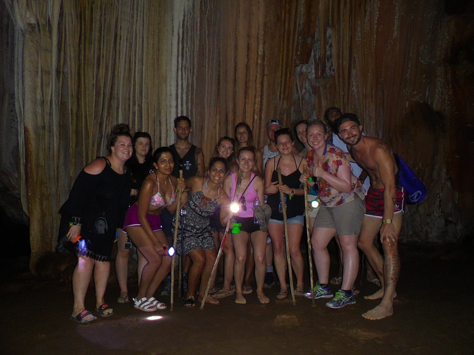 Caving group with headlamps and walking sticks gathers inside a dim cavern.