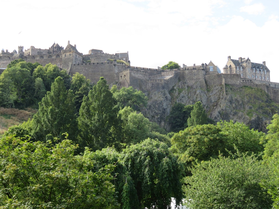 Vue d'un château historique au sommet d'une colline rocheuse, entouré d'une végétation luxuriante.