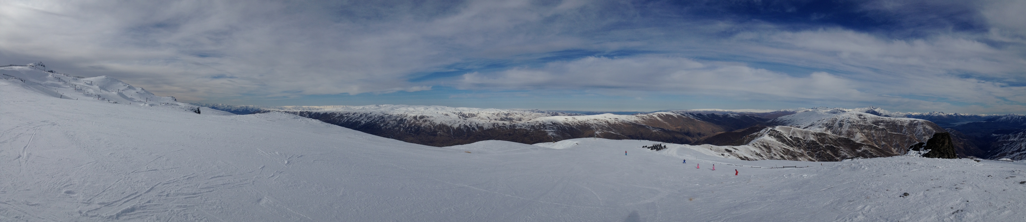 Vaste terrain enneigé avec des montagnes lointaines et un ciel partiellement nuageux.