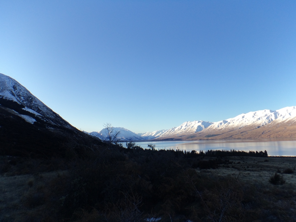 Vastes montagnes enneigées avec un lac au premier plan sous un ciel bleu clair.