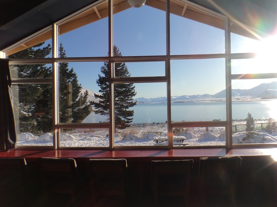 Vue à travers de grandes fenêtres d'un paysage enneigé avec un lac et des montagnes.