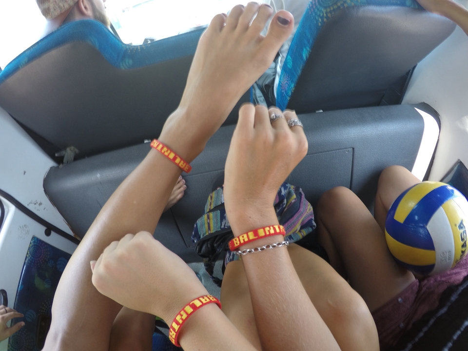 Close-up of travellers’ forearms showing colourful Bali wristbands inside a vehicle, volleyball in view.
