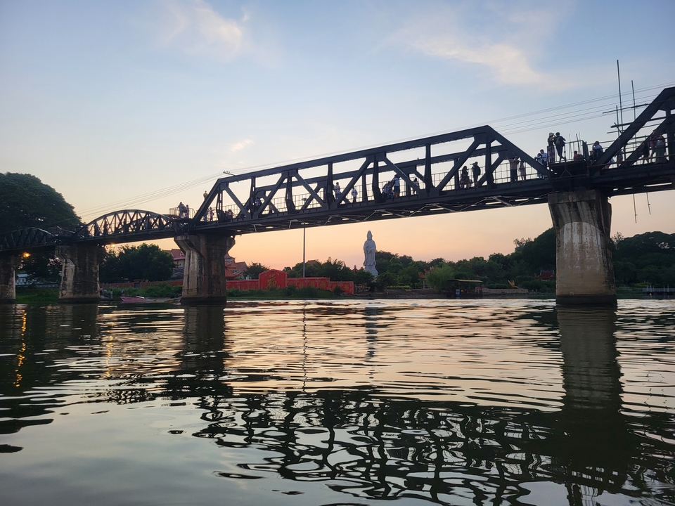 Bridge over a river with a large statue in the background during sunset.