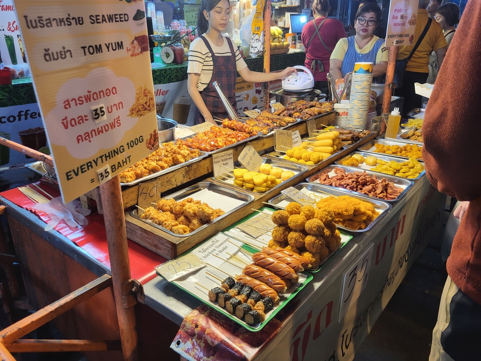 Food stall with various fried snacks and a sign with prices.