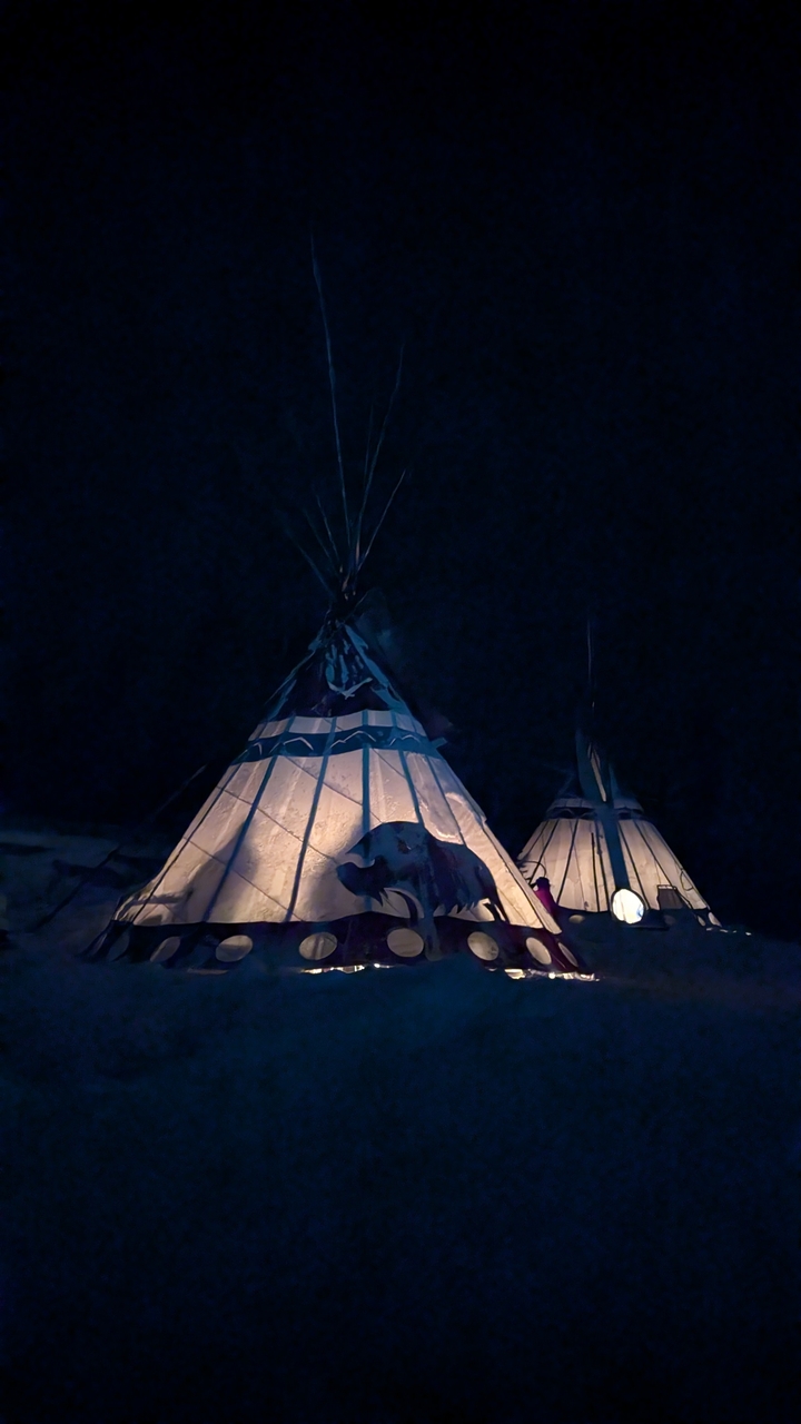 Illuminated traditional teepees glowing warmly against the dark winter night.
