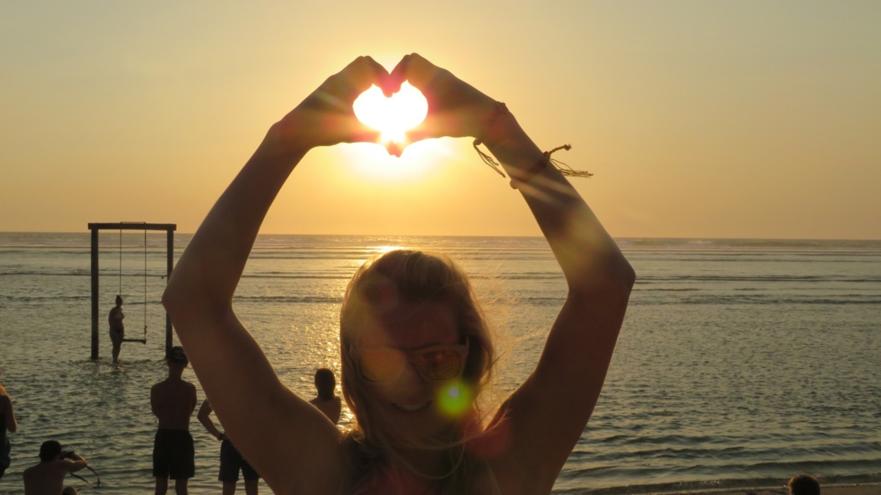 Person making a heart shape with hands at sunset.