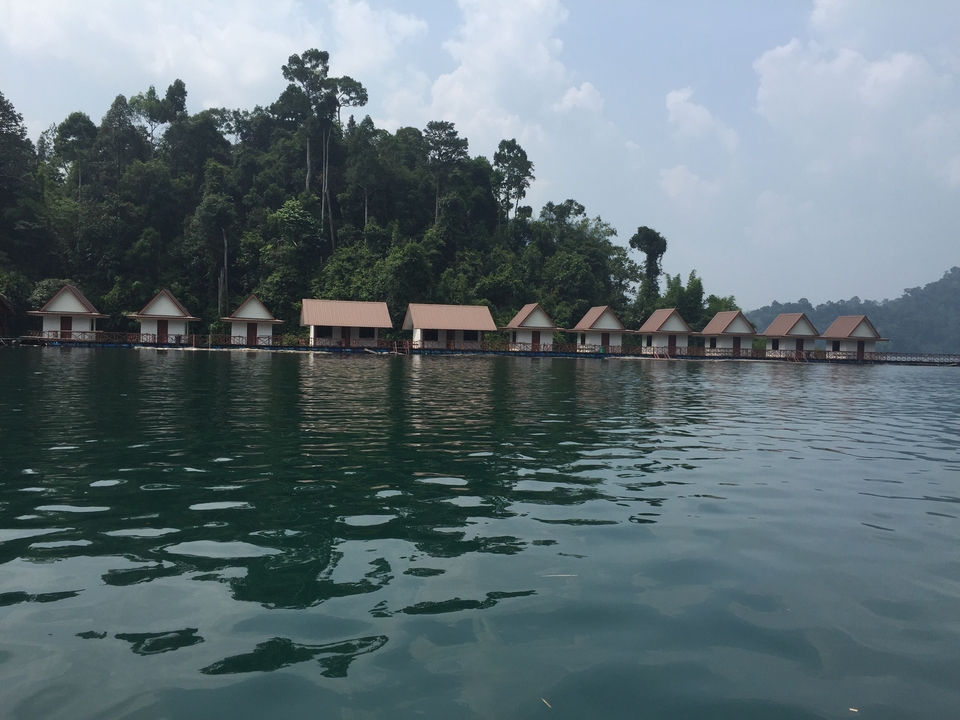 Line of floating cabin huts on a deep green lake surrounded by rainforest.