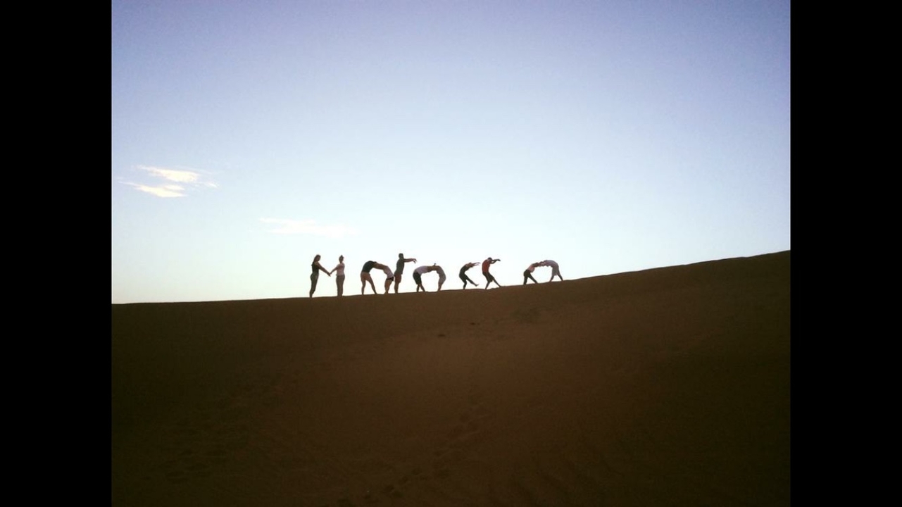 Silhouetten von Menschen, die bei Sonnenuntergang auf einer Sanddüne spazieren gehen.