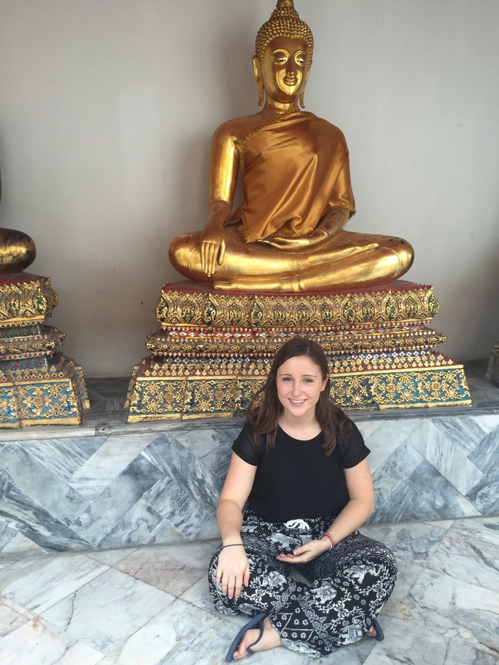 Traveller sitting in front of gilded seated Buddha statues at a Bangkok temple.