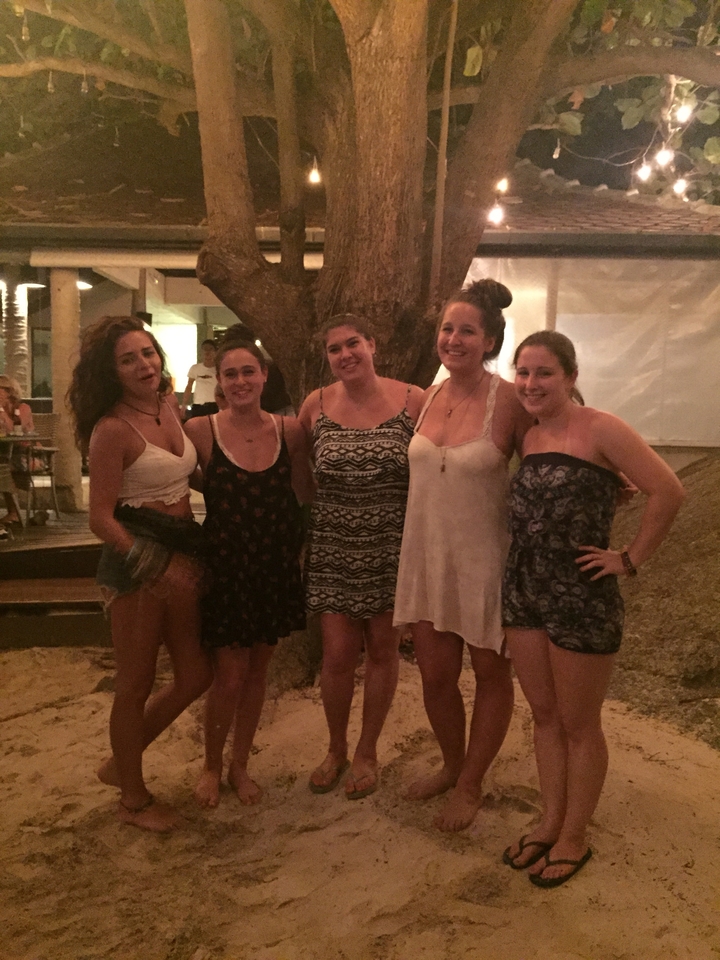 Five young women posing together in summer dresses at a beachside bar after dark.