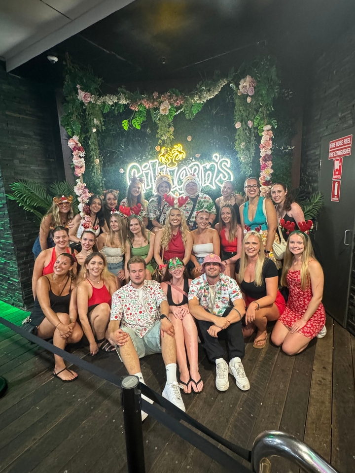 Un grand groupe en tenue de fête posant à l'intérieur d'un lieu avec un éclairage décoratif.