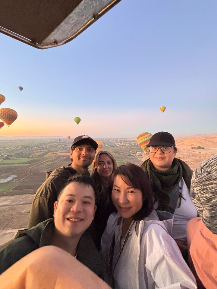 Groupe de personnes dans une montgolfière au-dessus d'un paysage au lever du soleil.