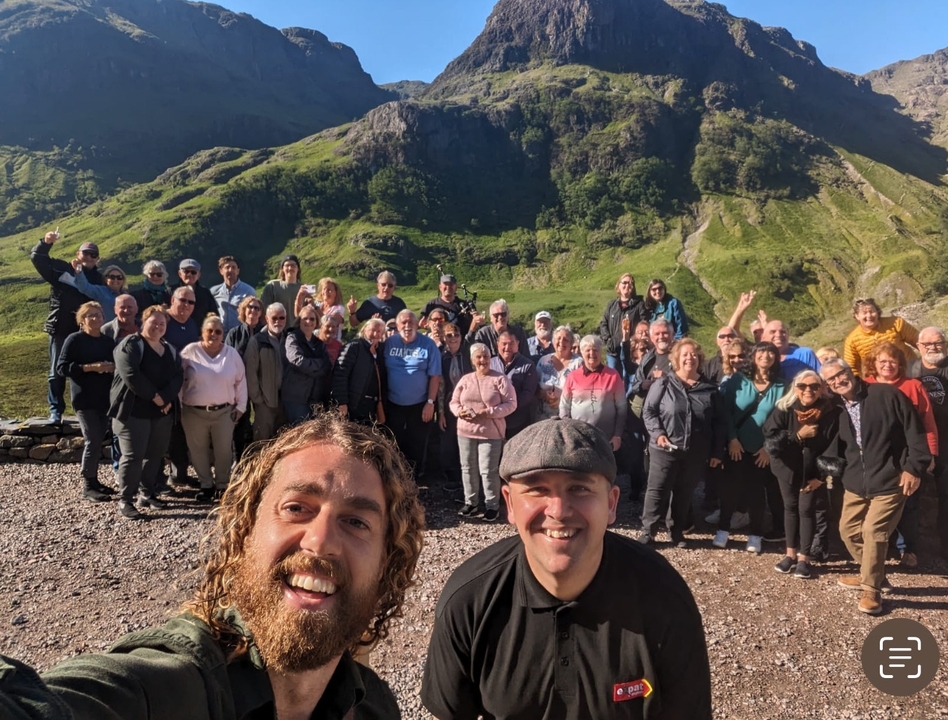Grand groupe de personnes souriantes devant un paysage de montagnes vertes.