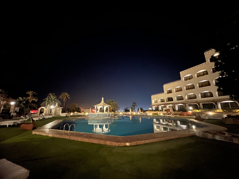 Vue nocturne d'un hôtel avec une piscine et des palmiers.