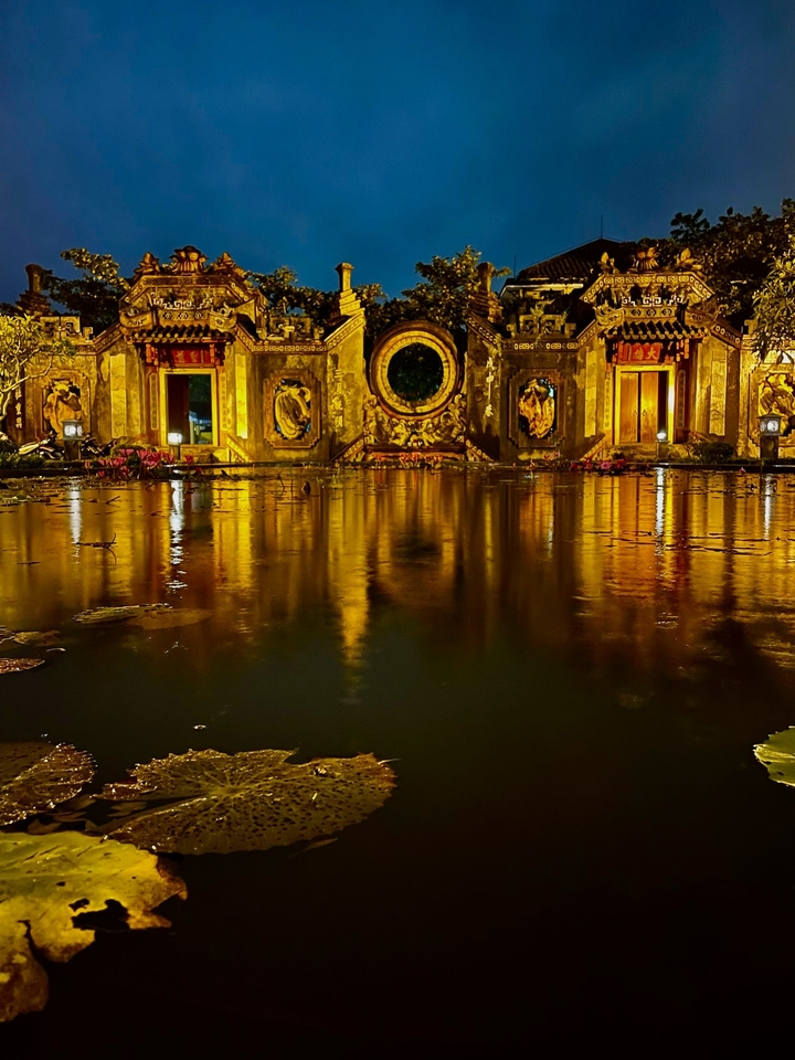 Bâtiment vietnamien décoré se reflétant dans l'eau la nuit.