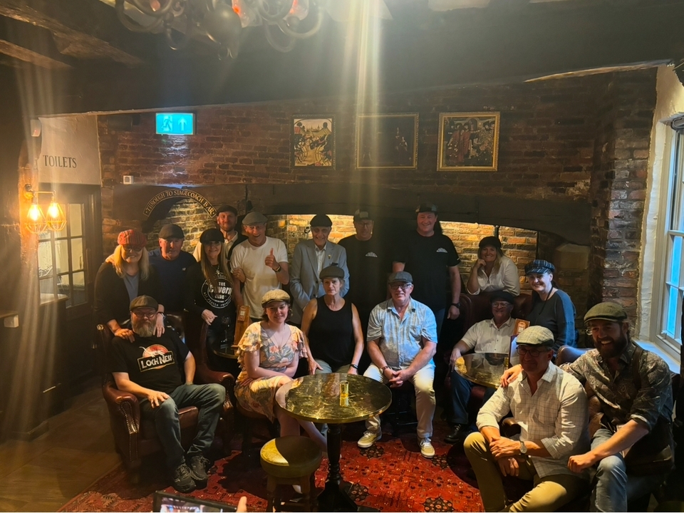 A large group of people in a dimly lit pub wearing hats and posing together.