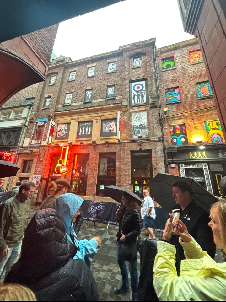 People walking with umbrellas in front of a vibrant, mural-adorned building.