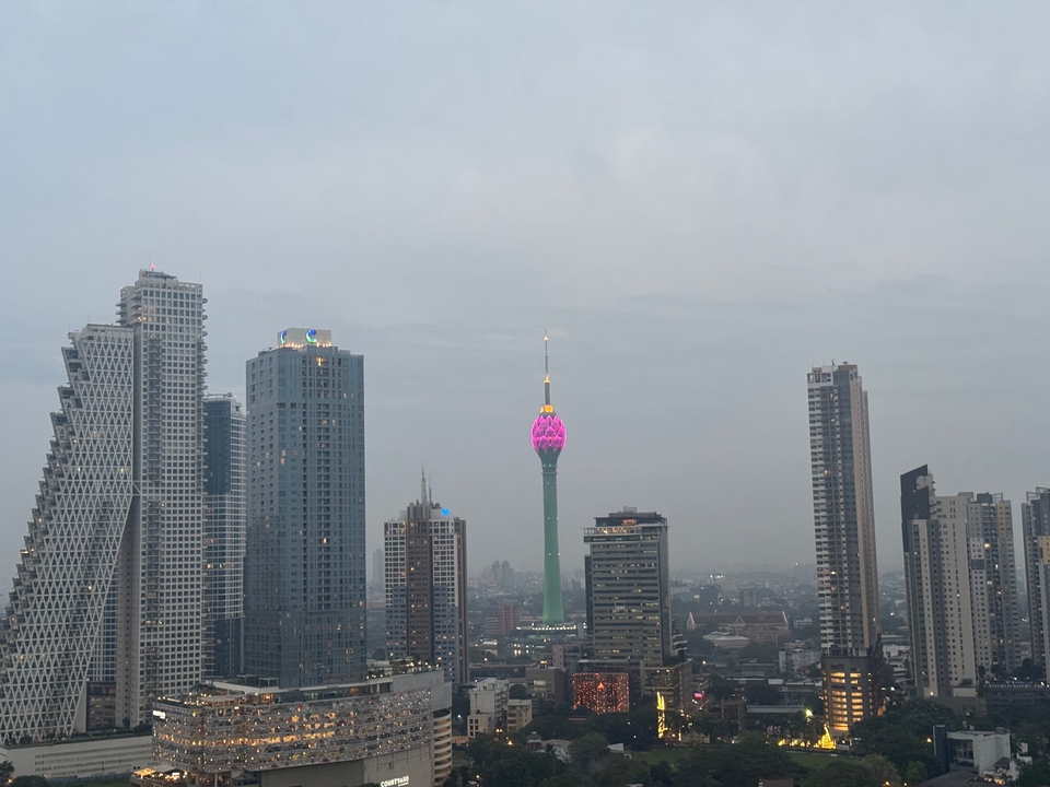 Horizonte de una ciudad con una torre iluminada prominente al atardecer.