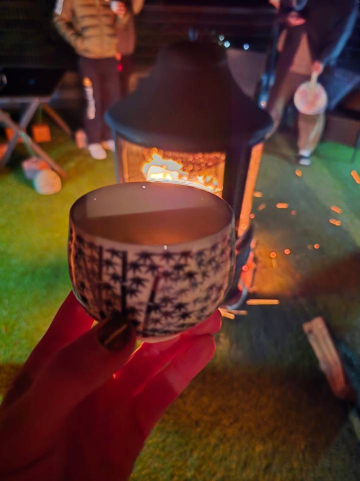 Tasse de boisson à la main avec une cheminée en arrière-plan.