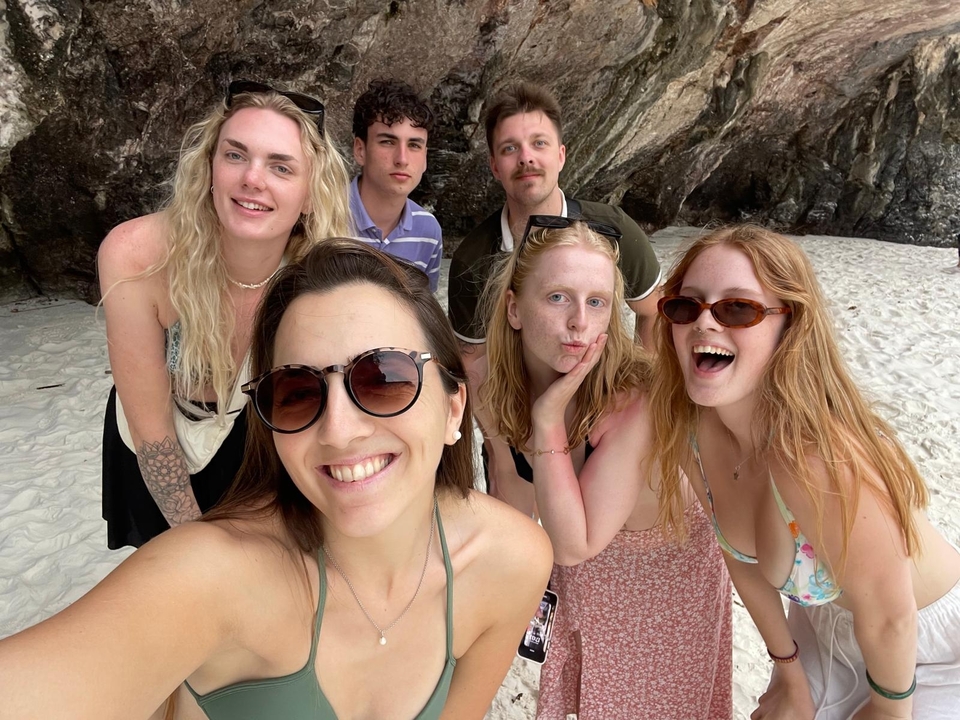 Un groupe d'amis qui posent sur une plage de sable blanc avec des falaises rocheuses à proximité.
