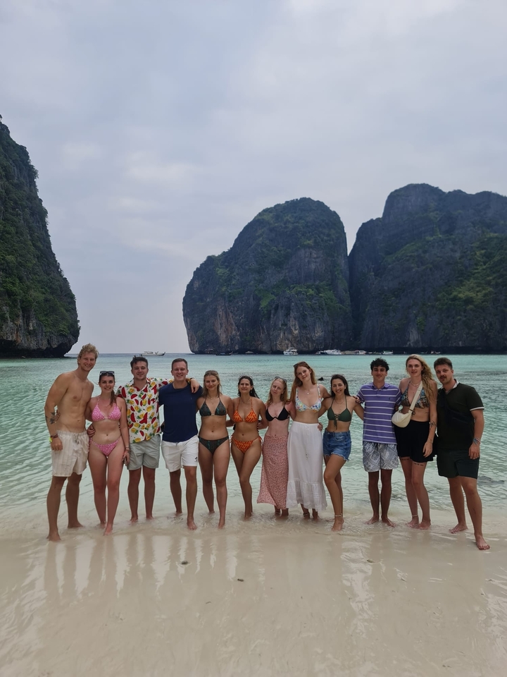 Un groupe de personnes posant sur une plage avec une eau claire et des falaises saisissantes en arrière-plan.