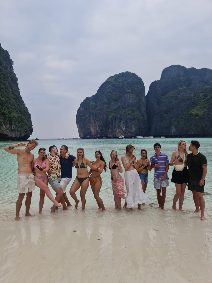 Un groupe d'amis qui prennent la pose de manière ludique sur une plage avec une eau turquoise claire.