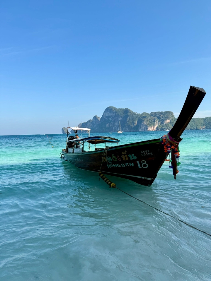 Un bateau à longue queue ancré dans des eaux bleu clair avec un paysage montagneux en arrière-plan.