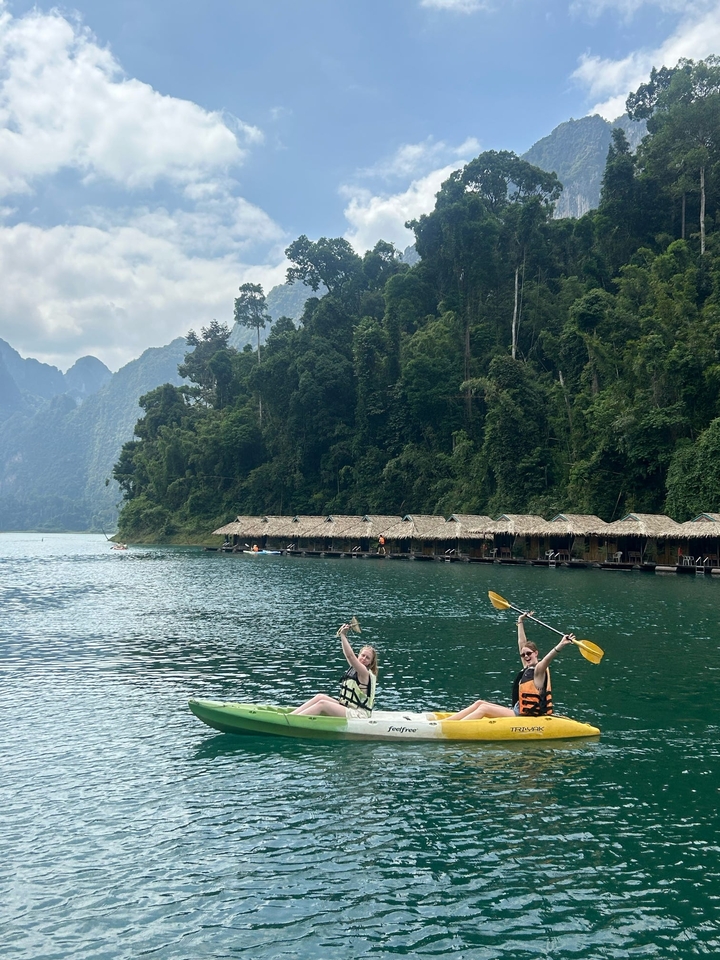 Deux personnes faisant du kayak sur un grand lac avec des bungalows flottants et des montagnes.