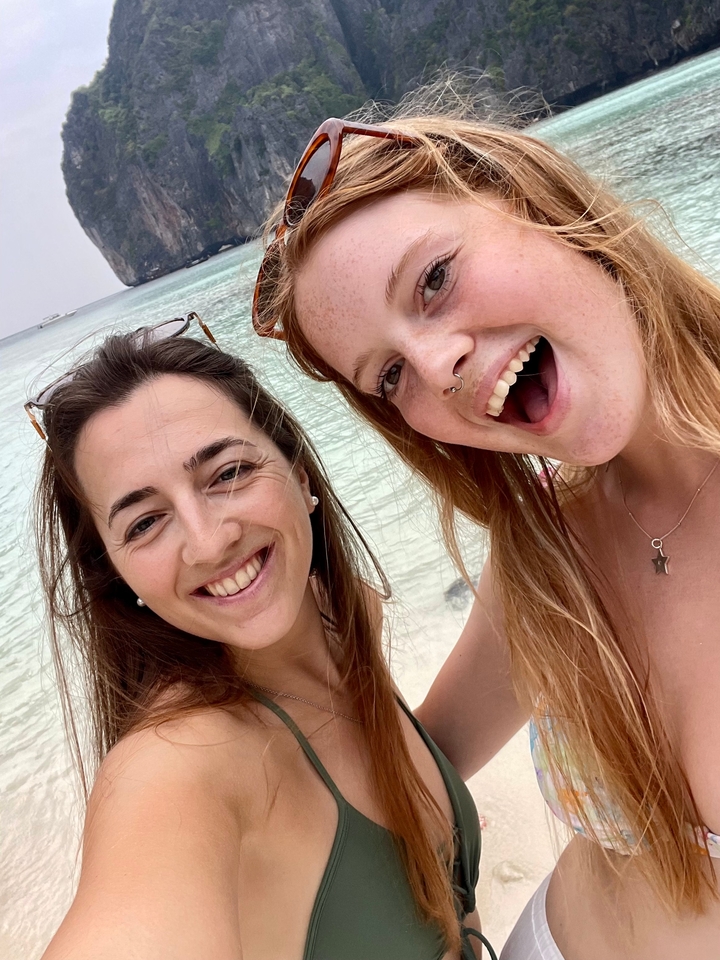 Deux amis qui posent et sourient sur une plage de sable avec une eau claire.