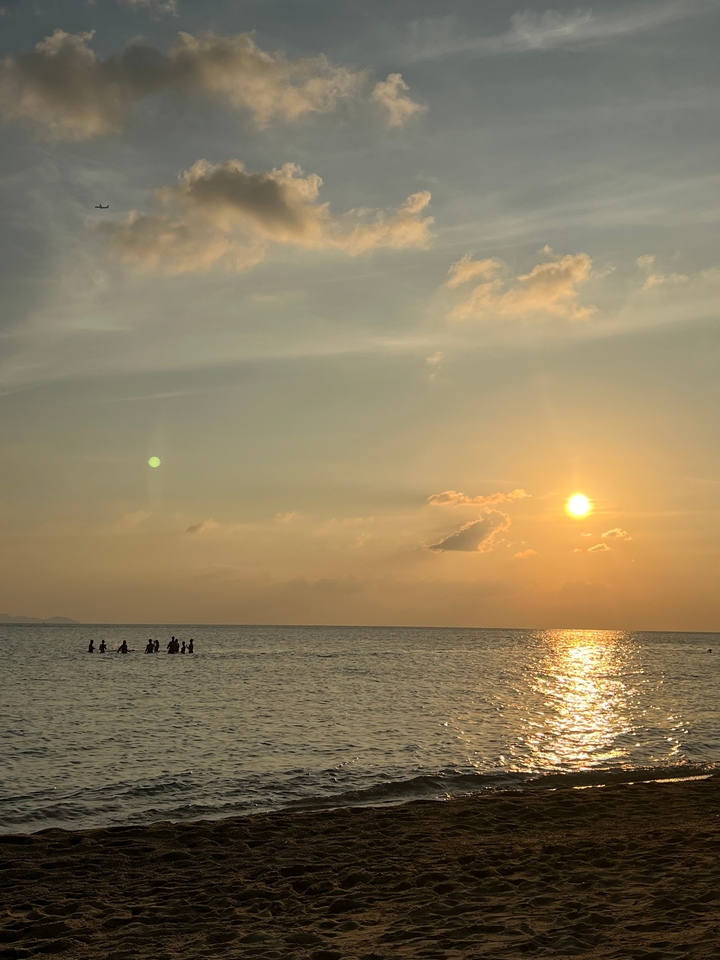 Silhouette de personnes marchant dans l'océan au coucher du soleil avec un ciel vibrant.
