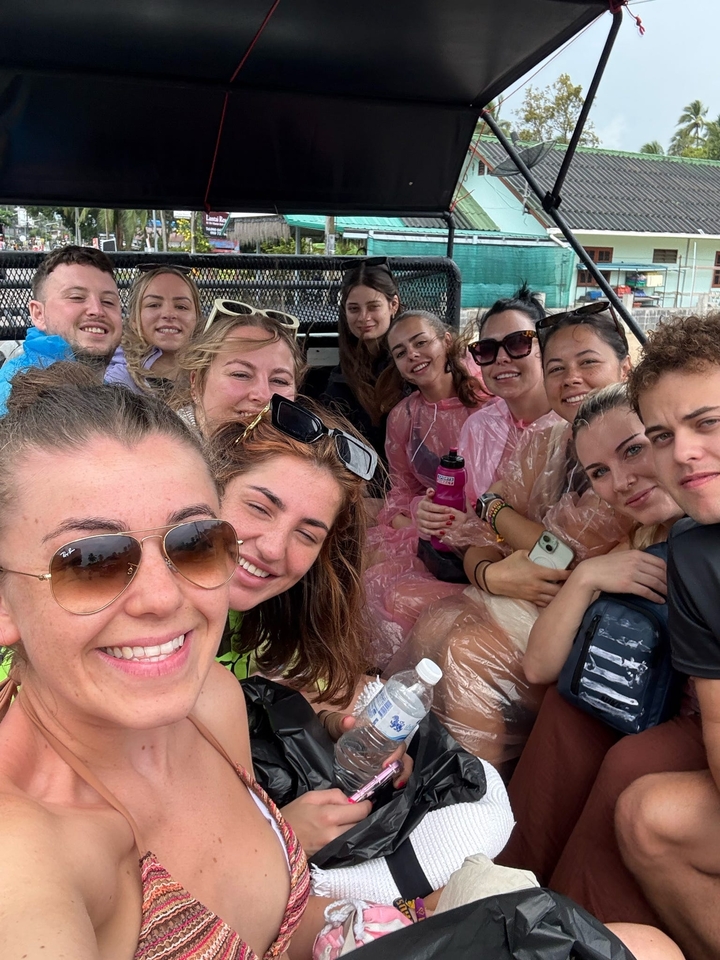 Un groupe de personnes prenant un selfie, certaines portant des ponchos, dans un cadre extérieur.