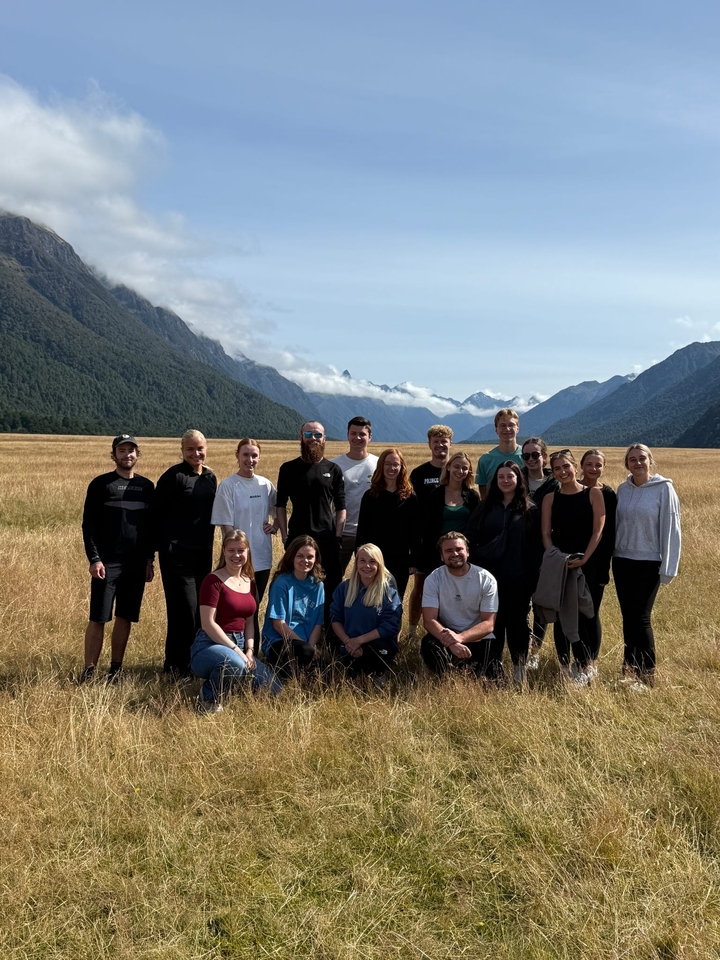 Groupe de personnes posant devant des montagnes et un champ.