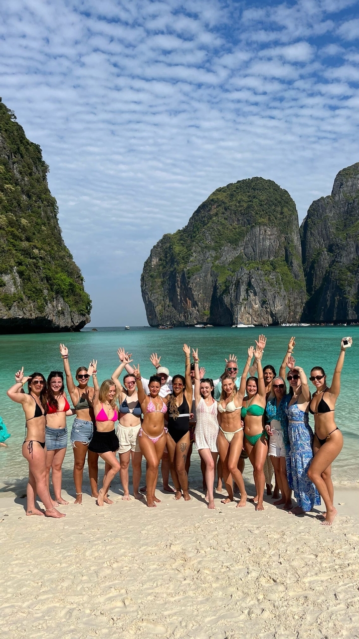 Grand groupe de personnes en maillots de bain sur une plage tropicale avec des falaises calcaires.