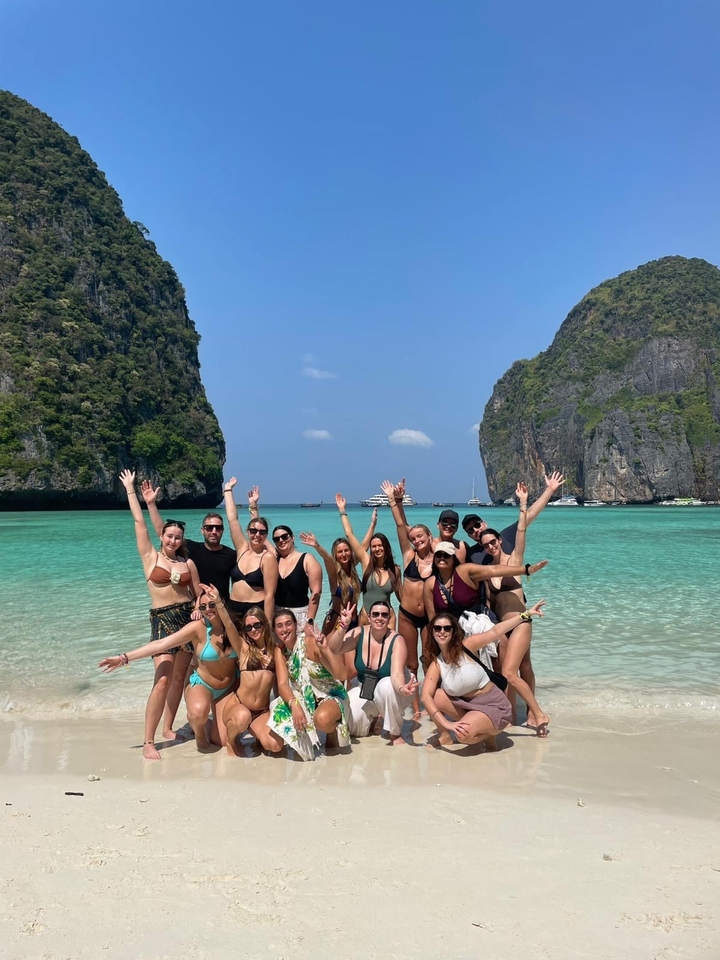Groupe de personnes posant sur une plage avec une eau claire et des falaises calcaires.